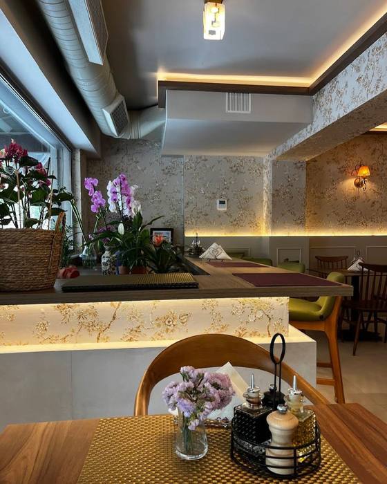 Orkide dhe lule mbi banak, salla pas tyre — orchids on the counter, the dining room beyond